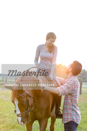 Smiling couple horseback riding in rural pasture