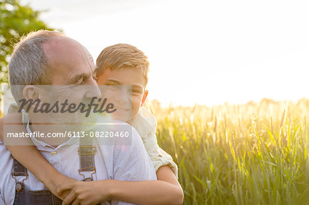 Portrait affectionate grandson hugging grandfather in rural wheat field