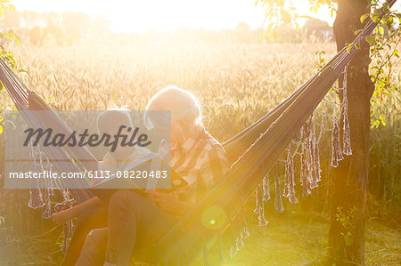 Grandmother and grandson reading book in sunny rural hammock