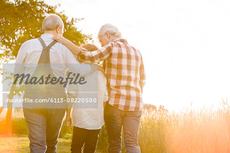 Affectionate grandparents and grandson walking along sunny rural wheat field