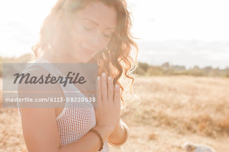 Serene boho woman with hands at heart center in sunny rural field