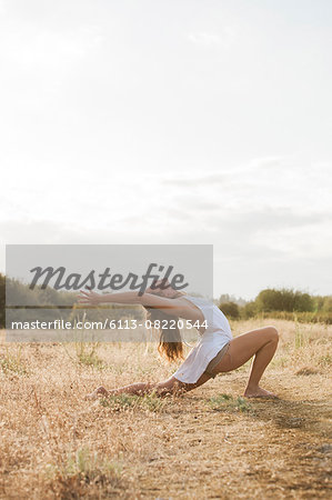 Boho woman in high crescent lunge yoga pose in sunny rural field