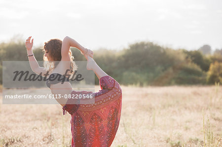 Boho woman in king dancer yoga pose in sunny rural field