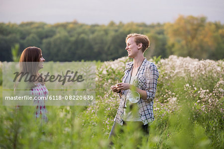 Two women standing in a meadow surrounded by tall grass and wild flowers.