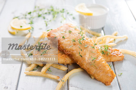 Fish and chips. Fried fish fillet with french fries on bright wooden background. Fresh cooked with hot smoke.