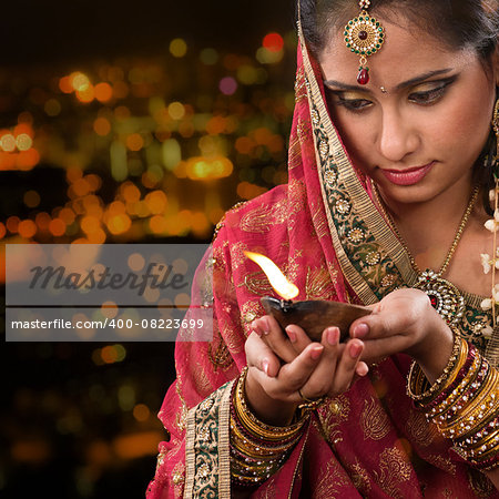 Indian female in traditional sari lighting oil lamp and celebrating Diwali or deepavali, fesitval of lights at temple. Woman hands holding oil lamp, beautiful lights bokeh background.