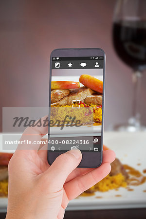 Female hand holding a smartphone against front view of couscous dish with meat and red wine