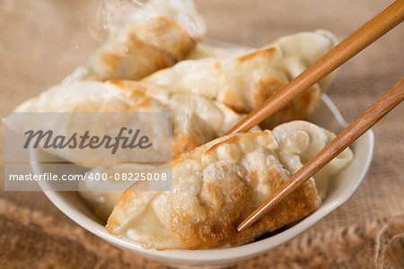 Close up fresh pan fried dumplings on bowl with chopsticks and hot steams. Asian food on rustic vintage wooden background.