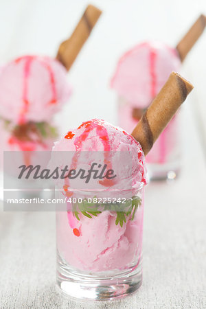 Scoops strawberry ice cream in glass cup with waffle on wooden vintage table background.