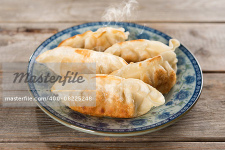 Fresh pan fried dumpling on plate. Chinese cuisine with hot steams on rustic vintage wooden background. Fractal on the plate is generic print.