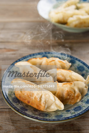 Fresh pan fried dumpling on plate. Chinese food with hot steams on rustic vintage wooden background. Fractal on the plate is generic print.