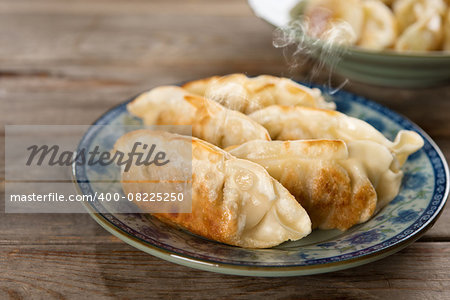 Fresh pan fried dumpling on plate. Chinese dish with hot steams on rustic vintage wooden background. Fractal on the plate is generic print.