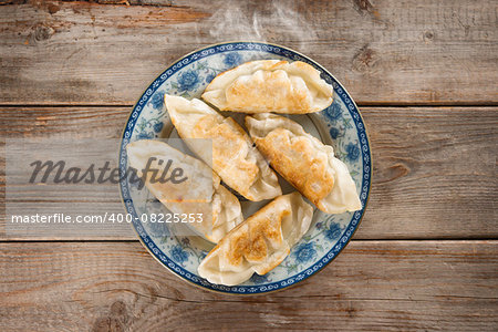 Top view fresh pan fried dumpling on plate. Chinese dish with hot steams on rustic vintage wooden background. Fractal on the plate is generic print.