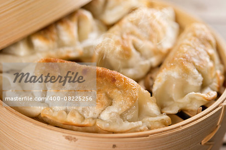 Close up fresh pan fried dumpling on bamboo basket. Chinese food with hot steams on rustic vintage wooden background.