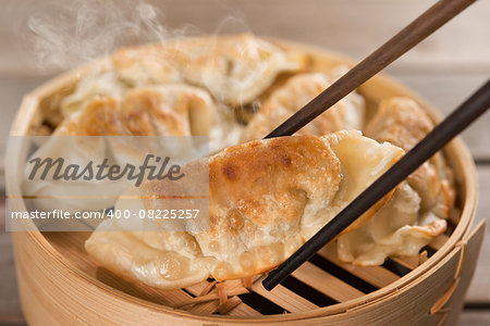 Fresh pan fried dumpling on bamboo basket with chopsticks. Chinese food with hot steams on rustic vintage wooden background.