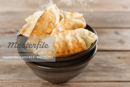 Close up fresh pan fried dumplings on bowl. Chinese dish with hot steams on rustic vintage wooden background.
