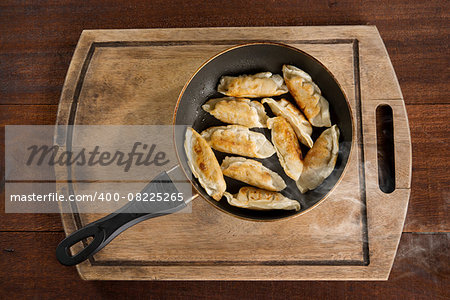 Top view cooking fried dumplings in a frying pan. Chinese food with hot steams, on rustic vintage wooden background.