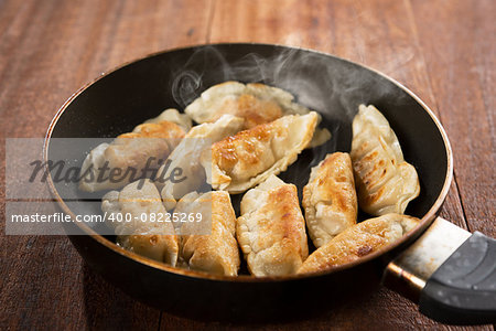 Close up cooking fried dumplings in a frying pan. Chinese food with hot steams, on rustic vintage wooden background.