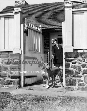 1930s UPSCALE SPORTY WOMAN WITH TWO FOX HOUND DOGS ON A LEASH BY KENNEL GATE