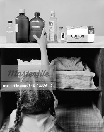 1960s LITTLE GIRL REACHING TO TOP SHELF FOR BOTTLE OF POISON