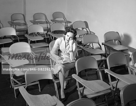 1950s WOMAN SITTING IN CLASSROOM OF EMPTY CHAIRS ANNOYED