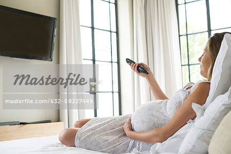 Pregnant woman watching TV on bed