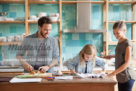 Young daughter drawing at kitchen counter while parents prepare meal