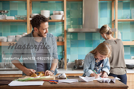 Young daughter drawing ar kitchen counter while parents prepare meal