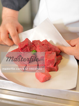Butcher wrapping meat cubes in wax paper, cropped