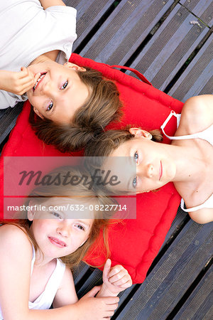 Girls lying down outdoors with heads resting on shared cushion