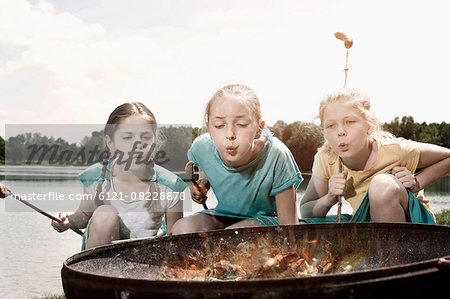 Three friends preparing sausages on camp fire, Bavaria, Germany