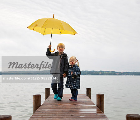 Children with yellow umbrella on dock