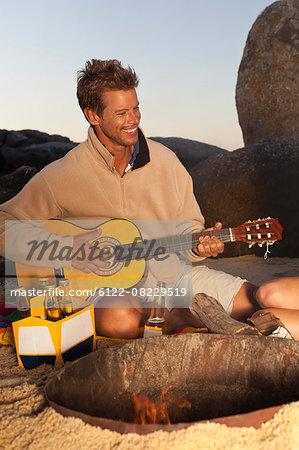 Man playing guitar with beer on beach