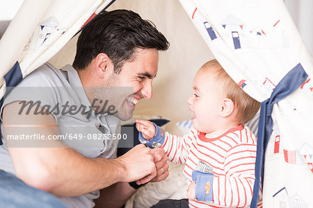 Father and young son sitting in play tent indoors, laughing together