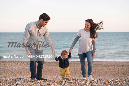 Young family walking along pebble beach hand in hand