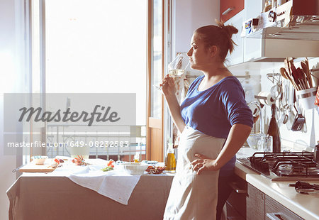 Mid adult woman taking a cooking break and drinking white wine in kitchen