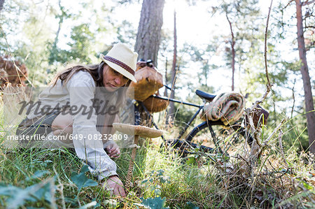 Mature woman with bicyle foraging for mushrooms in forest