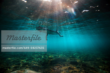 Underwater view of surfer waiting on a shallow reef for a wave in Bali, Indonesia