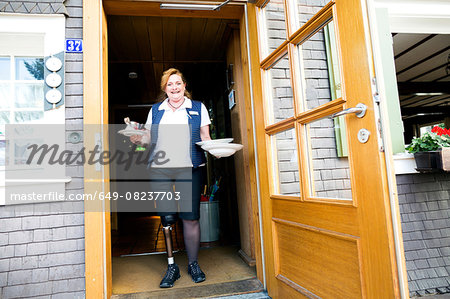 Mid adult woman with prosthetic leg, standing in doorway holding plates