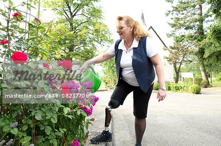 Mid adult woman with prosthetic leg, in garden, watering plants
