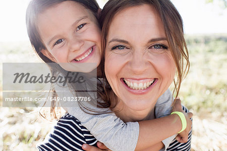 Portrait of mature woman giving daughter piggy back in park