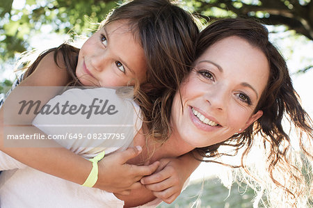 Portrait of mature woman giving daughter piggy back in park