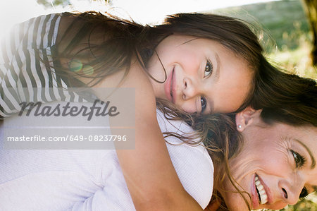 Mature woman giving daughter piggy back in park