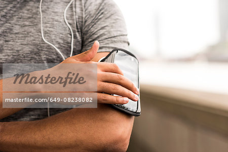 Cropped shot of male runner choosing music on smartphone armband