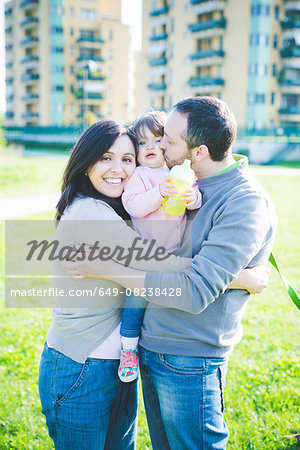 Portrait of mid adult couple kissing toddler daughter in park