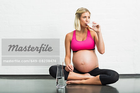 Full term pregnancy young woman drinking water whilst practicing yoga