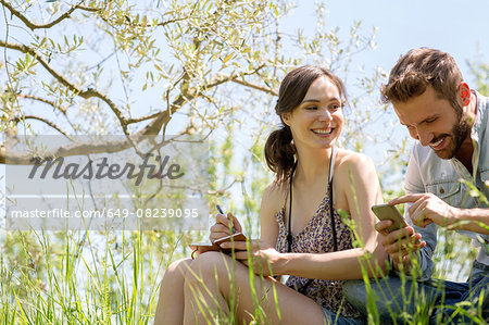 Low angle view of young couple sitting looking down at smartphone smiling