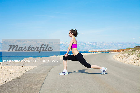 Young woman stretching leg on waterfront path