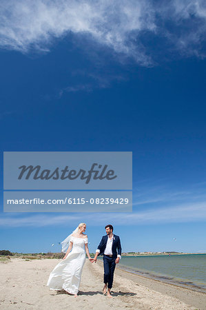Bride and bridegroom walking happily on beach
