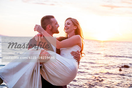 Groom carrying bride on pebble beach at sunset Groom carrying bride on pebble beach at sunset